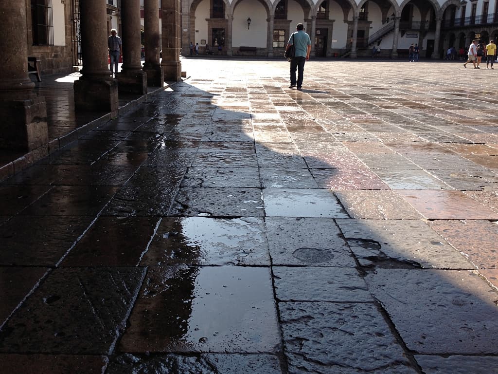 Wet stone and the arcade shadow across the zócalo after the rain cleared