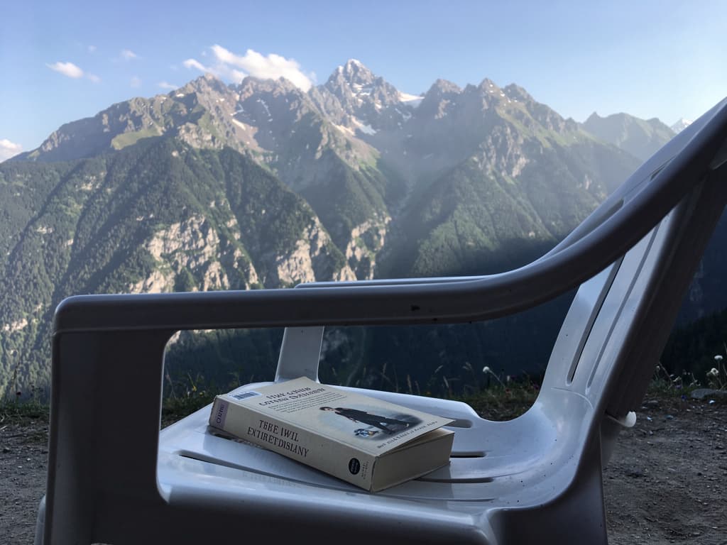 Finished paperback on the plastic chair, mountains behind, mid-morning light