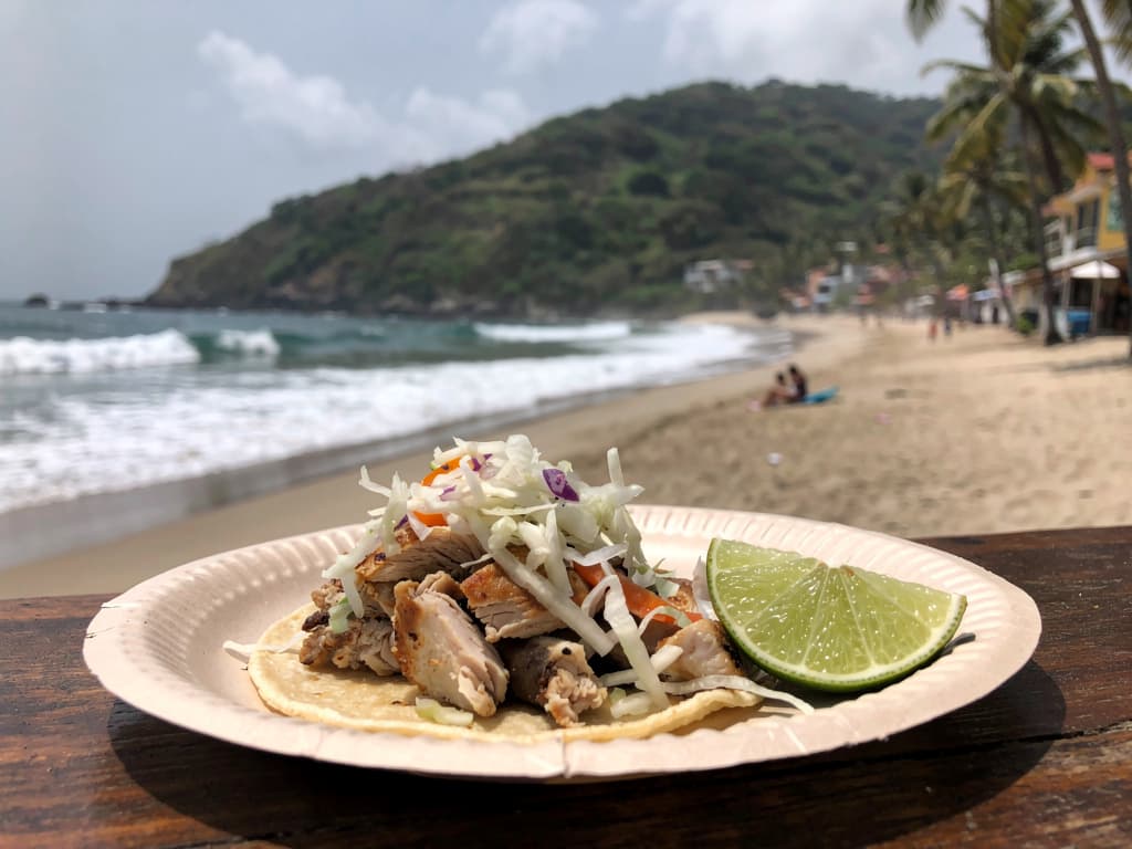 Pescado taco on a paper plate, cabbage, lime squeezed, stand two blocks off the beach.